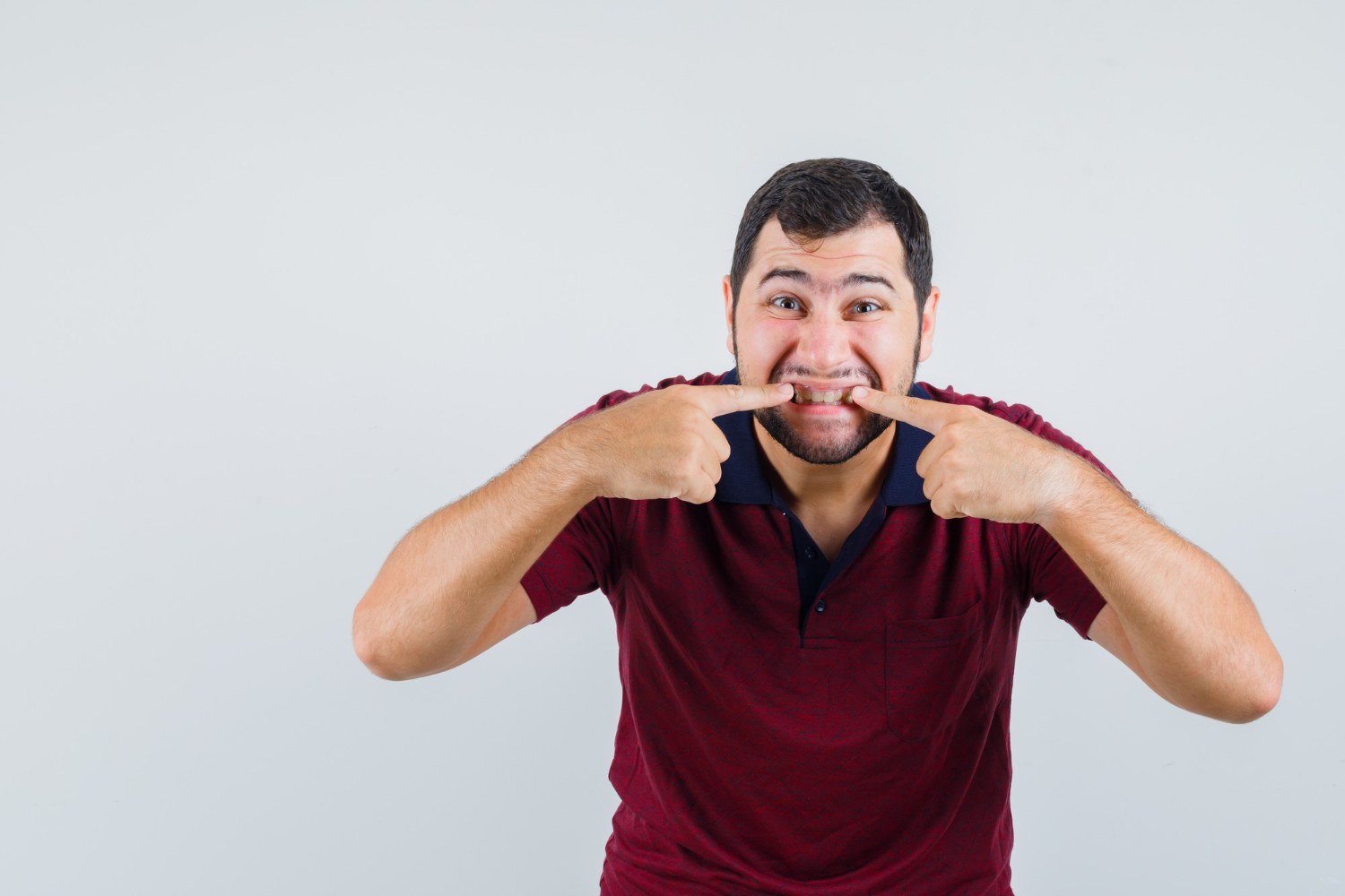 Young male pointing at his teeth in red t-shirt , front view
