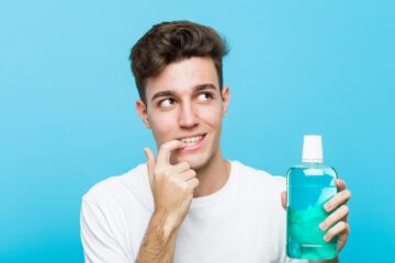 young caucasian man holding mouthwash relaxed thinking about something